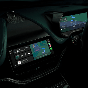 The interior of a car showing a digital dashboard with navigation maps and a center touchscreen displaying maps, music controls, and calendar events in a modern, dark-themed layout inspired by recent Apple feature announcements.