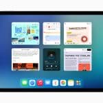 An iPad screen running iPadOS 26 displays six open app windows—notes, music, reminders, and web pages—in a multitasking view over a blue gradient background, with a dock of app icons at the bottom.