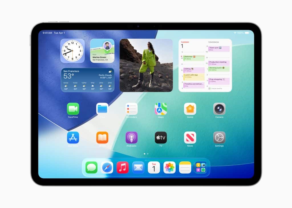 A tablet running iPadOS 26 displays a home screen with app icons and widgets—clock, weather, calendar, and photo—set against a blue and teal gradient background.