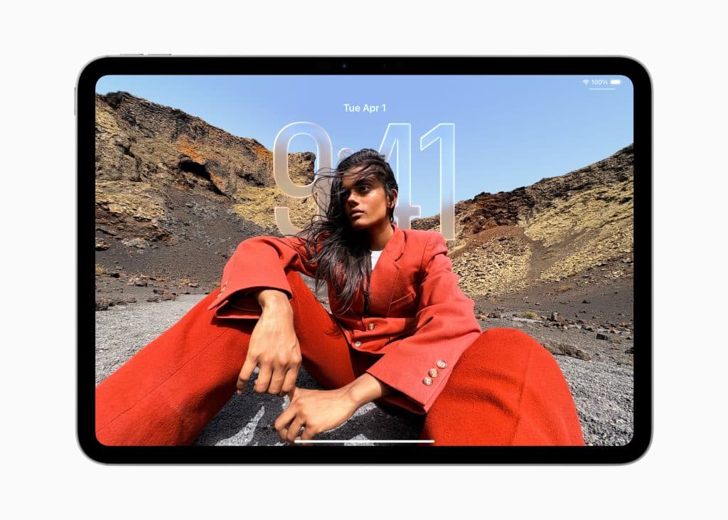 A woman in a bold red suit poses outdoors on rocky terrain, seated with one knee up against a dramatic landscape. The image is displayed on a tablet running iPadOS 26, showing the time 9:41 and date Tue Apr 1.