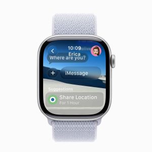 Apple Watch running watchOS 26 displays an iMessage with Erica—"Where are you?"—and options to share your location for 1 hour, all set against a backdrop of serene sand dunes.