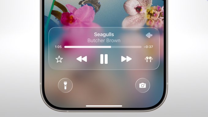 Close-up of a smartphone screen with Liquid Glass Design, showing music playback controls for "Seagulls" by Butcher Brown. Flashlight and camera icons appear at the bottom, set against a floral wallpaper, running on iOS 26.
