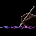 A hand holding an Apple Pencil draws colorful, swirling lines in shades of purple, blue, and pink on a dark background.