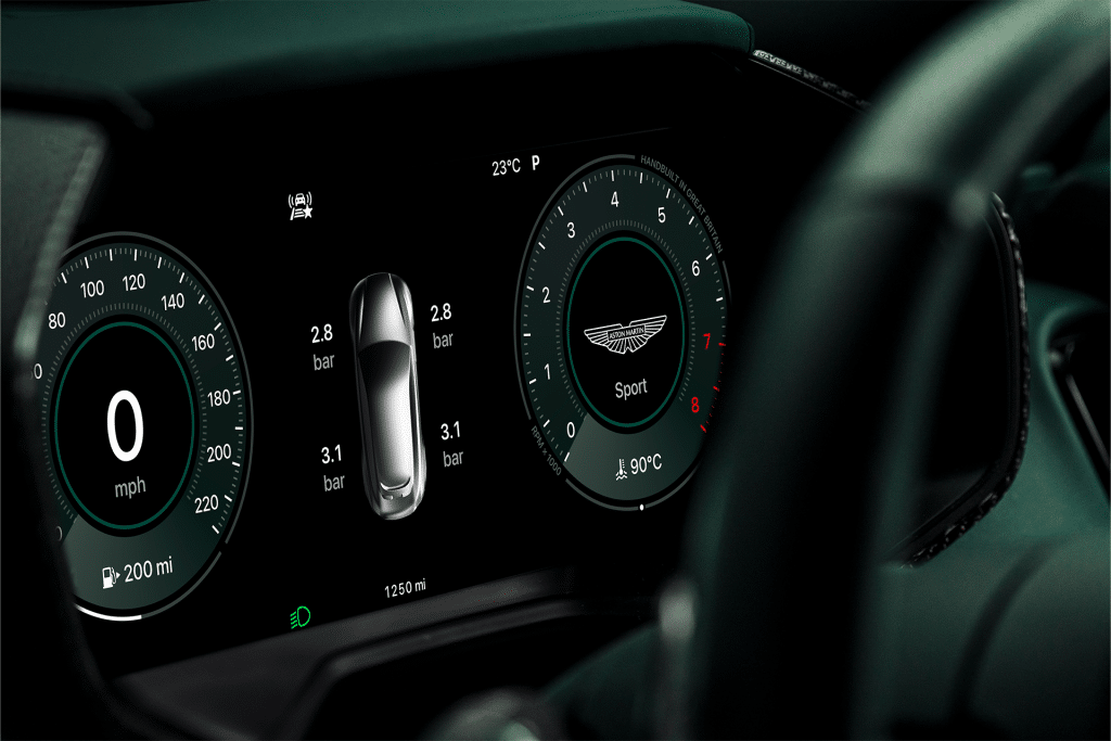 A digital car dashboard display shows 0 mph speed, tire pressures, a central car graphic, “Sport” mode with the Aston Martin logo, Carplay Ultra integration, a temperature of 23°C, and various dashboard indicators.