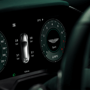 A digital car dashboard display shows 0 mph speed, tire pressures, a central car graphic, “Sport” mode with the Aston Martin logo, Carplay Ultra integration, a temperature of 23°C, and various dashboard indicators.