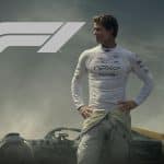 A race car driver in a white racing suit stands before a Formula 1 car with the F1 logo above him. Smoky, dramatic lighting sets an intense competitive mood, reminiscent of an F1 haptic trailer's immersive energy.