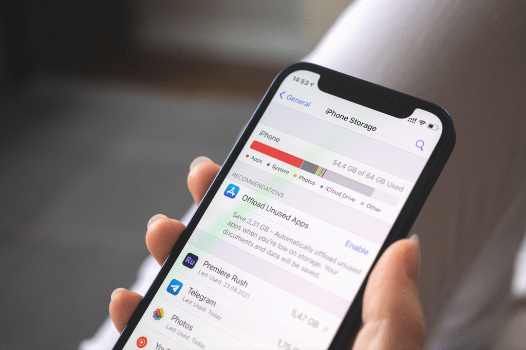 A hand holding an iPhone displays the Storage screen, highlighting usage by apps, photos, and system files, with helpful suggestions to offload unused apps.