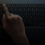 A hand with dark skin presses the escape key on a backlit laptop keyboard in a dimly lit environment, highlighting how essential shortcuts can boost productivity for iPad power users.