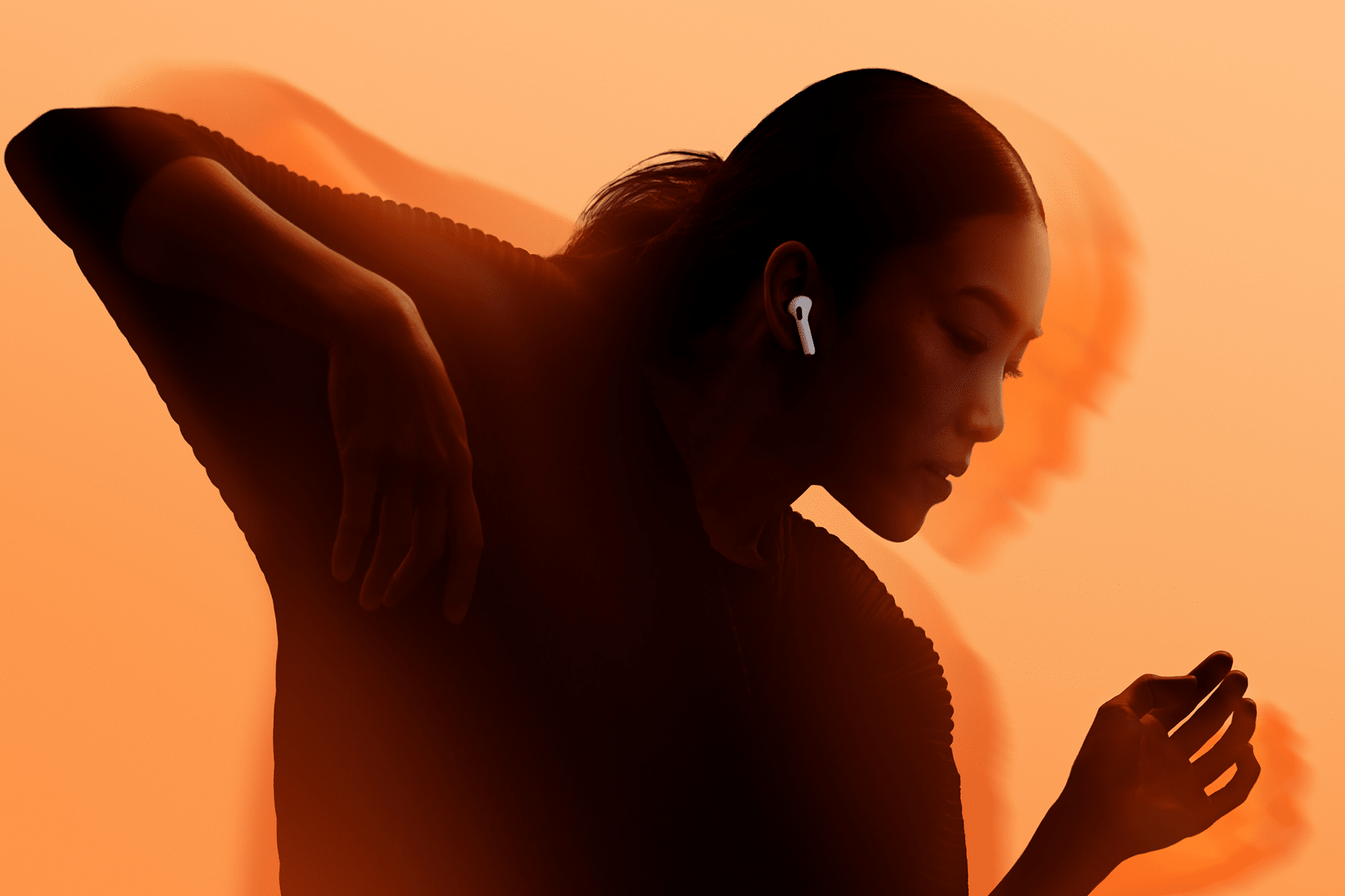 A person with long hair in a ponytail wears AirPods, showcasing an immersive audio experience as they move gracefully against an orange background, with motion blur emphasizing movement and expression.