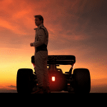 A racecar driver in a racing suit stands next to a formula car at sunset, the dramatic orange sky hinting at scenes from the upcoming Apple F1 Movie, with the car’s taillights illuminated.