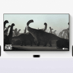 A TV screen with tvOS 26 displays a "Prehistoric Planet" scene on Apple TV+, showing large dinosaurs. Two AirPlay Speakers flank the TV, all set on a white surface—perfect for an immersive home theater experience.