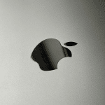 Close-up of a metallic surface featuring a reflective Apple logo in the center, evoking Mac Studio's focus on desktop productivity and streamlining, with minimal text along the right edge.