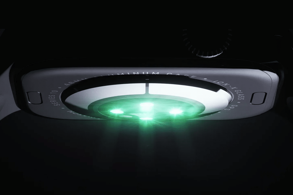 Close-up of the underside of an Apple Watch with green sensor lights illuminated, highlighting the device's blood oxygen monitoring sensors and part of the engraved text around its circular sensor area.