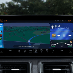 A car dashboard display featuring CarPlay Ultra shows navigation directions to Apple Park, music playing, and flight information. The screen includes a map, distance, estimated arrival time, and control icons. Trees are visible outside the windshield.