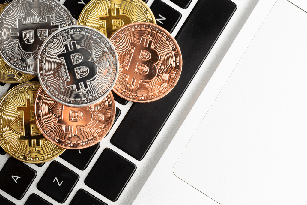 Several gold, silver, and bronze Bitcoin coins are placed on the black and white keyboard of a laptop, symbolizing digital currency and technology—a common scene among crypto startups often targeted by macOS malware.