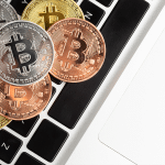Several gold, silver, and bronze Bitcoin coins are placed on the black and white keyboard of a laptop, symbolizing digital currency and technology—a common scene among crypto startups often targeted by macOS malware.