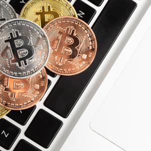 Several gold, silver, and bronze Bitcoin coins are placed on the black and white keyboard of a laptop, symbolizing digital currency and technology—a common scene among crypto startups often targeted by macOS malware.