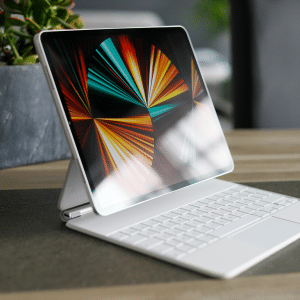 A tablet with a colorful abstract display is attached to a white keyboard and trackpad, positioned on a table beside a small pot of succulents.