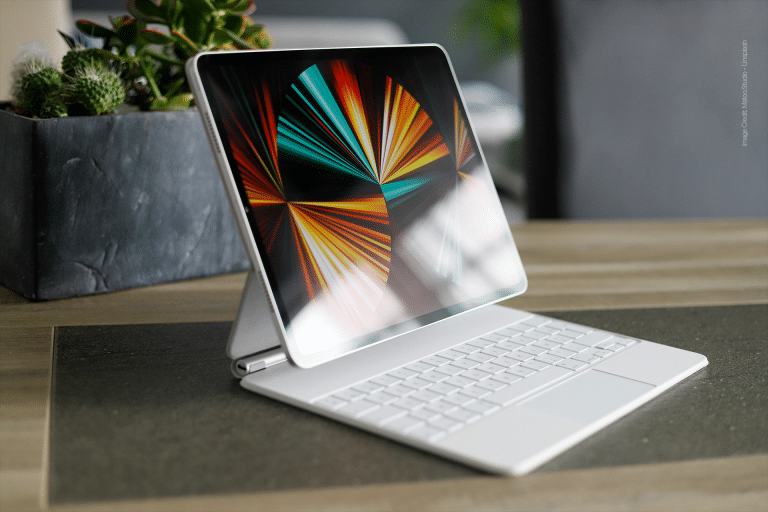 A tablet with a colorful abstract display is attached to a white keyboard and trackpad, positioned on a table beside a small pot of succulents.