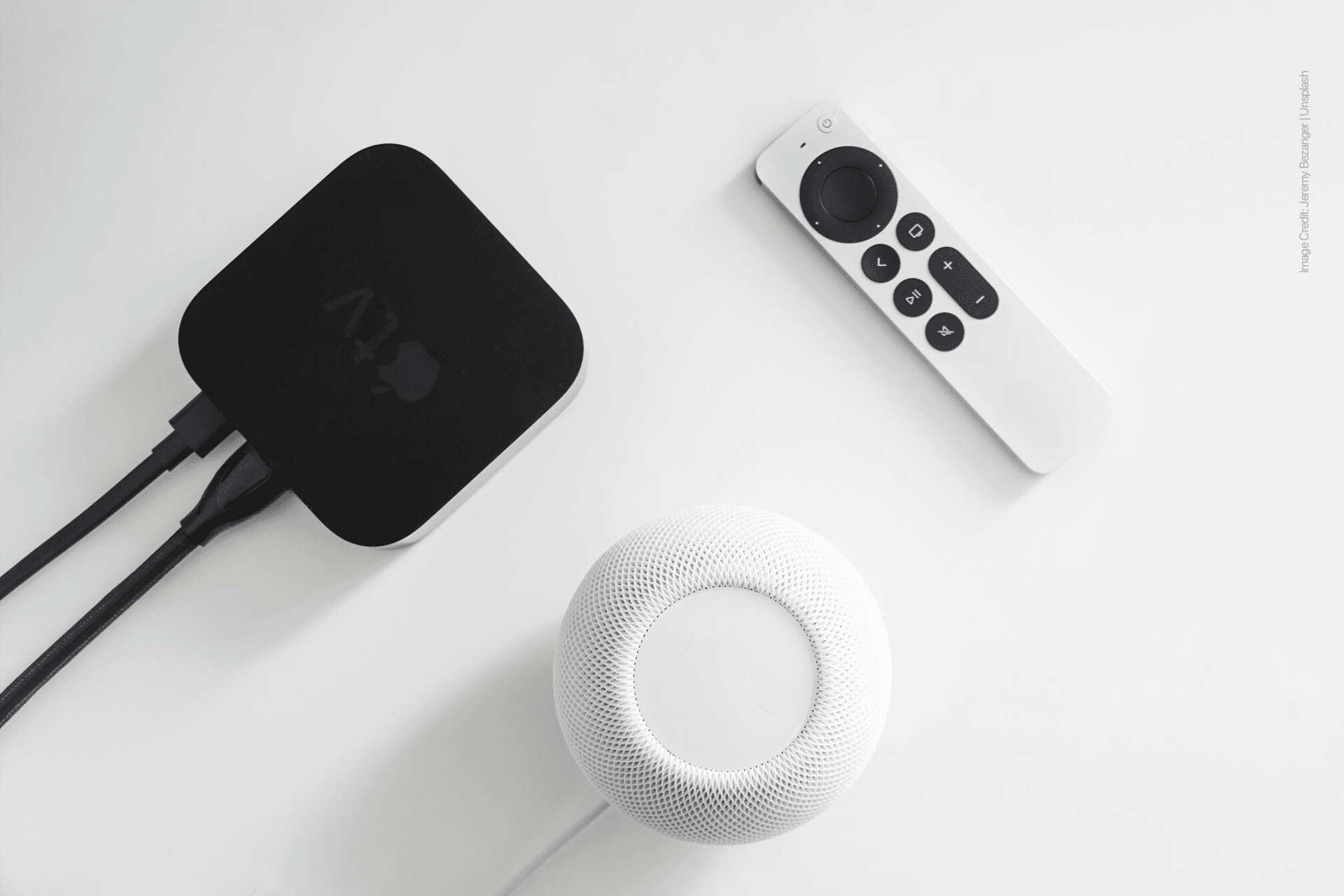 A black Apple TV box running tvOS 18.6 with connected cables, a white Apple TV remote, and a white Apple HomePod mini with HomePod 18.6 on a white surface.