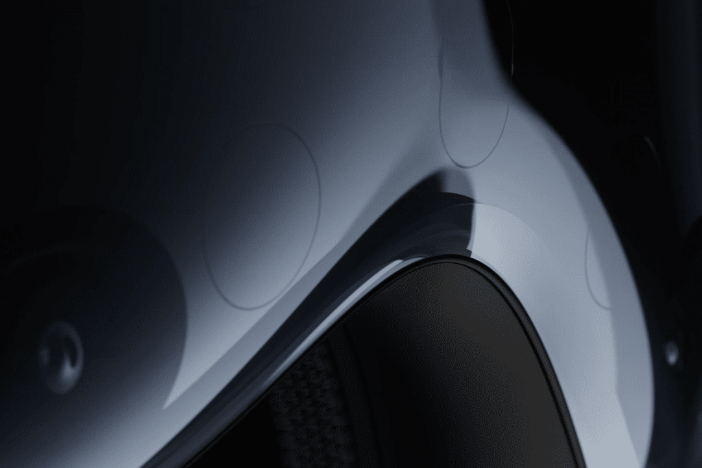 Close-up of a sleek, curved metallic car body with a glossy finish, highlighting the wheel arch and subtle reflections—its precision reminiscent of the advanced design behind Apple Vision Pro under soft lighting.