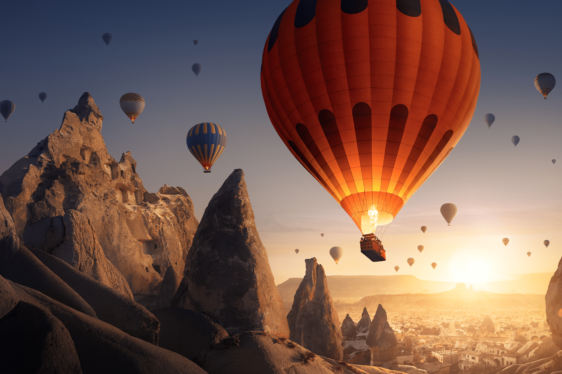 Hot air balloons float over rocky, pointed formations at sunrise in Cappadocia, Turkey. The clear sky and landscape bathed in a golden glow create a cinematic escape, like nature’s own home theatre at dawn.