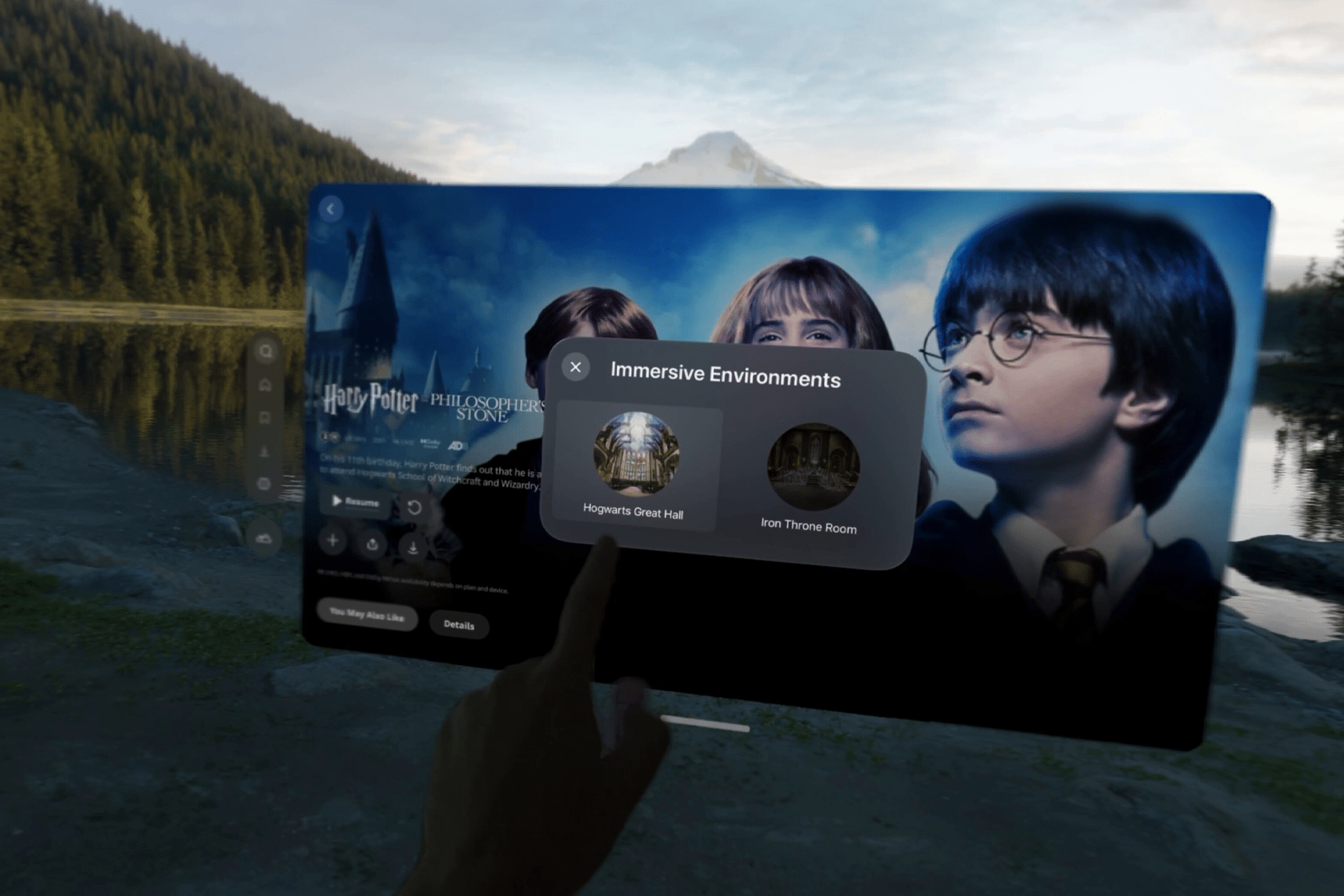 A hand points at a virtual Apple Vision Pro screen displaying “Immersive Environments” options from Harry Potter, with Hogwarts characters in the background and a scenic lake and mountain visible behind the transparent interface.