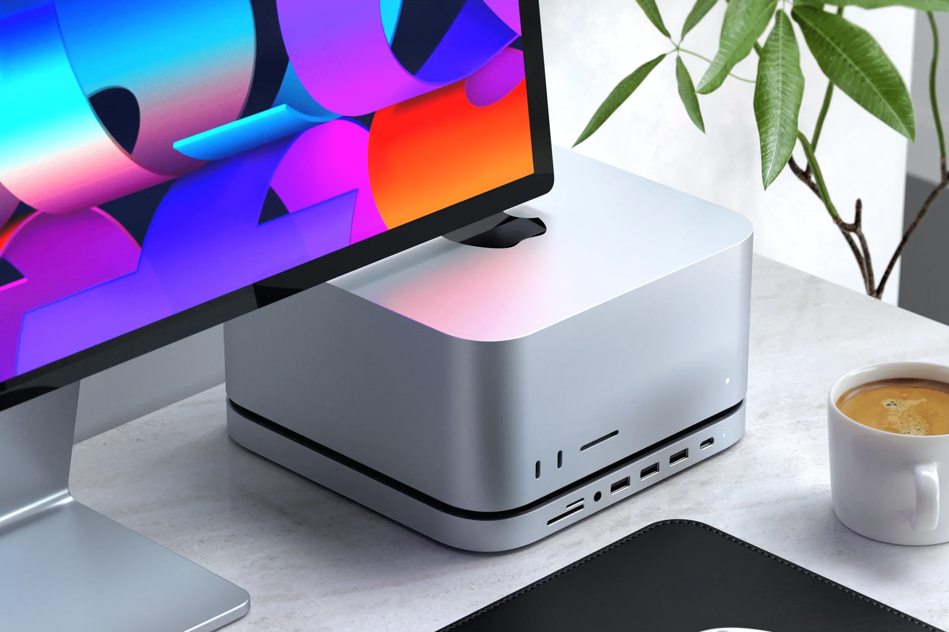 A close-up of a modern desktop setup featuring the new Mac Studio, a monitor with a colorful screen, a plant, and a cup of coffee on a white desk—perfect for ensuring a seamless transition when moving files between devices.