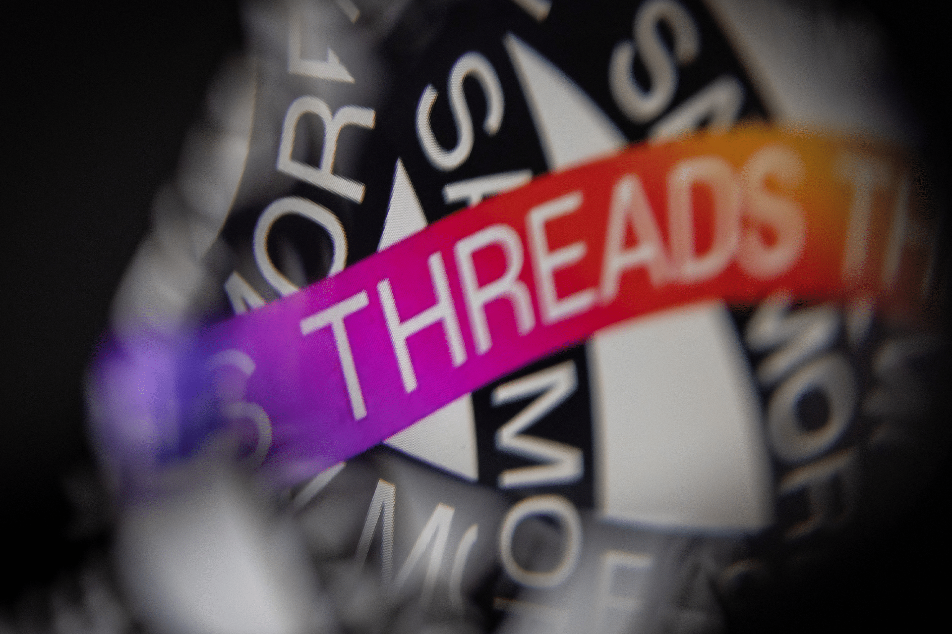 A close-up image featuring the word "Threads" in bold, white letters on a vibrant pink and orange gradient strip, with blurred black and white text in the background.