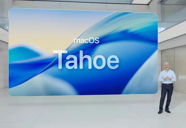 A person stands in front of a large screen displaying “macOS Tahoe Public Beta” with a blue abstract background in a modern, bright room, capturing the excitement of the latest innovation in Mac Computing.