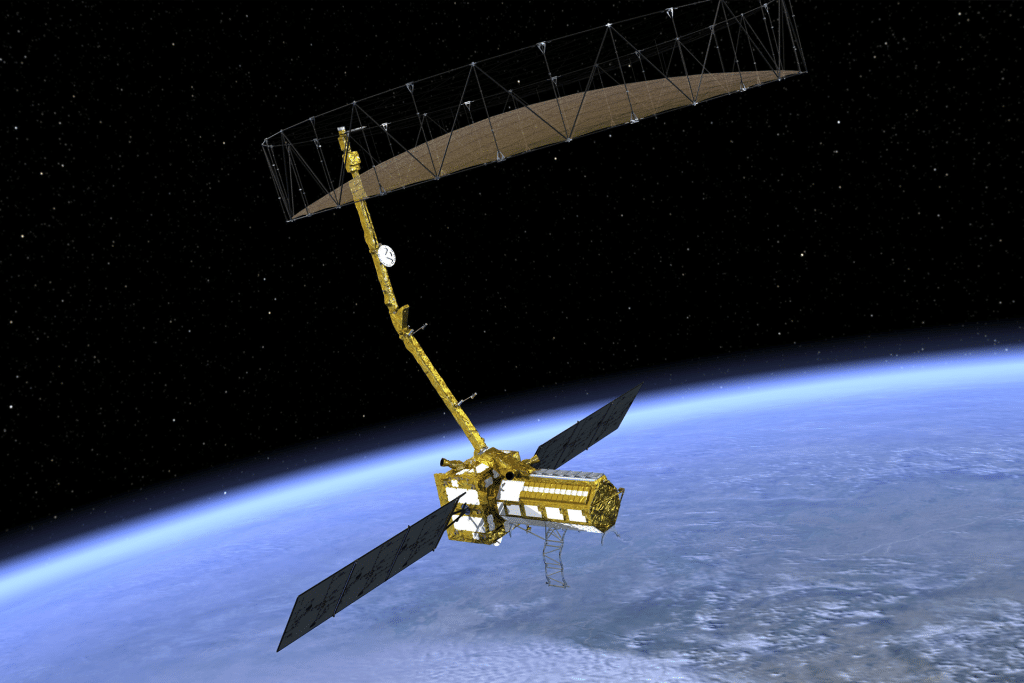 A gold-colored NISAR satellite with large solar panels and a wide radar antenna or reflector orbits above Earth against the dark backdrop of space.