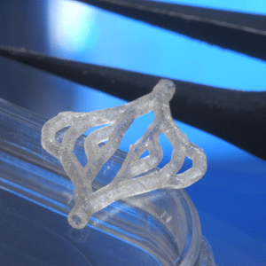 A close-up of a translucent, geometric 3D-printed artificial skin resting on the edge of a clear petri dish, with black tweezers in the background against a blue surface, highlighting innovation in regenerative medicine.