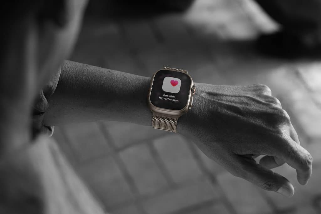 A person’s wrist wearing a smartwatch displaying a heart icon and the message “Possibly irregular rhythm,” suggesting the watch is monitoring heart health. The image is mostly black and white except for the watch screen.