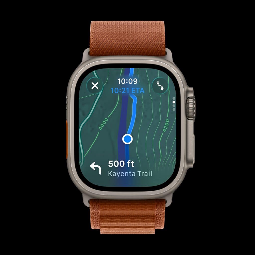 A smartwatch with an orange band displays a navigation map showing a blue route line, current location, direction to Kayenta Trail, 500 feet to next turn, and estimated arrival time of 10:21.