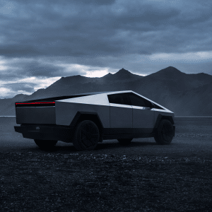 A futuristic, angular silver pickup truck equipped with Tesla Cybertruck modifications drives off-road on a dark, misty landscape with mountains in the background beneath a cloudy sky, ready for thrilling adventures.