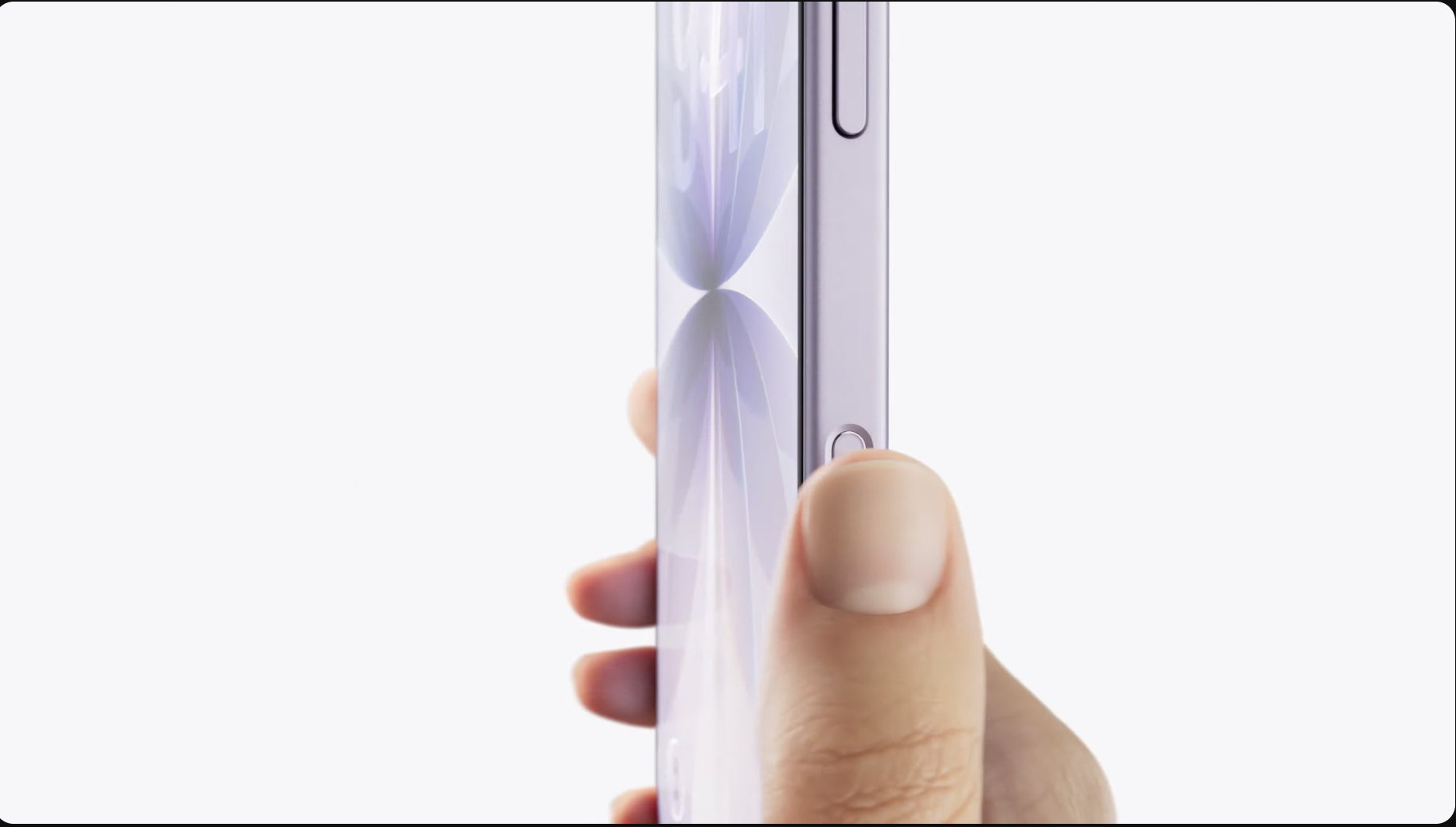 A hand holds a light purple iPhone 17 vertically, with a thumb pressing the side button. The phone’s sleek, reflective surface stands out against a plain white background.