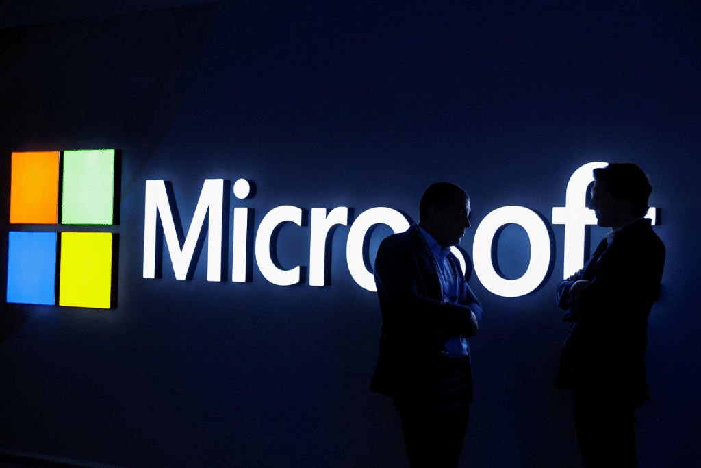 Two people stand in silhouette, talking in front of a brightly lit Microsoft logo on a dark background, highlighting the growing importance of AI infrastructure in today's tech landscape.