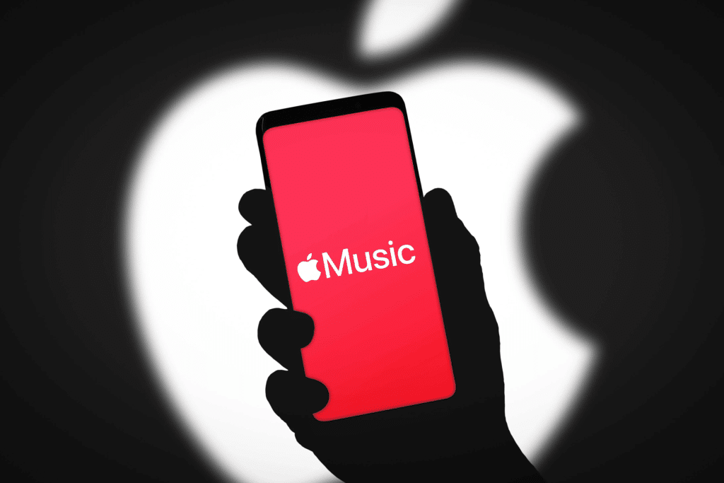 A hand holds a smartphone displaying the Apple Music app on a red screen, with a large blurred white Apple logo in the background, highlighting the swipe gesture used to switch tracks effortlessly.
