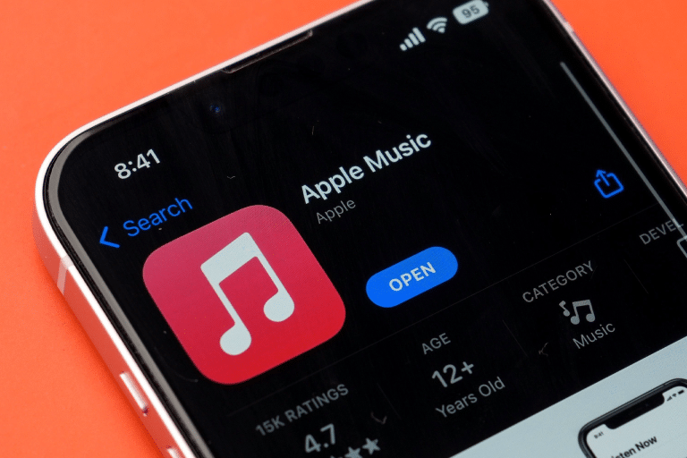 A smartphone screen displays the Apple Music app page in the App Store, featuring the app icon, “Open” button, ratings, age, and category on a bright orange background—now highlighting an iOS 26.1 new gesture for swiping to switch tracks.