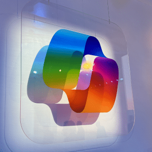 A colorful, translucent layered sculpture featuring overlapping shapes in blue, green, yellow, purple, and orange—like a visual Microsoft Copilot AI tutorial—suspended against a white background with soft lighting and subtle reflections.