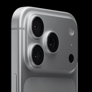 Close-up of the top corner of a silver smartphone, showcasing the advanced iPhone 17 Pro camera with three lenses, a flash, and a small sensor on a sleek, metallic surface against a black background.
