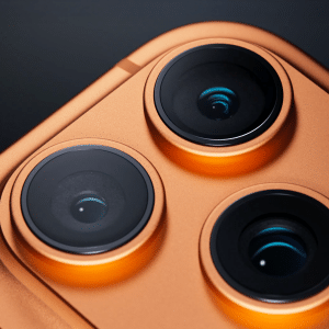 Close-up of three camera lenses on the back of an orange smartphone, highlighting its metallic finish and modern design—perfect for capturing stunning shots with the iPhone 17 Pro camera system.