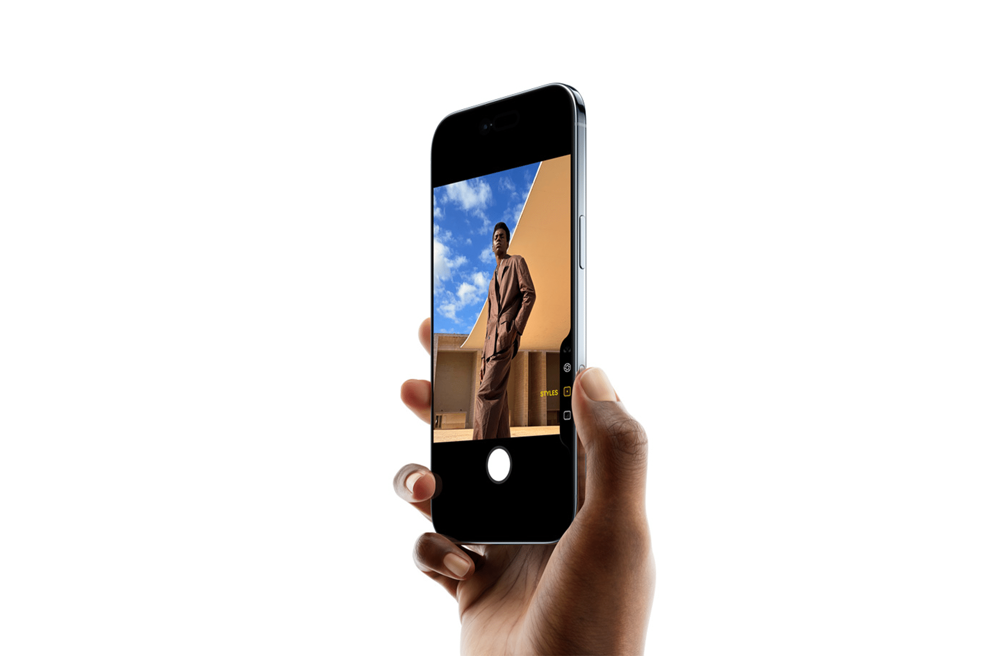 A hand holds an iPhone 17 Pro displaying a photo of a person in a brown outfit standing outdoors against a blue sky and tan building, with the camera app interface visible after a recent software update.