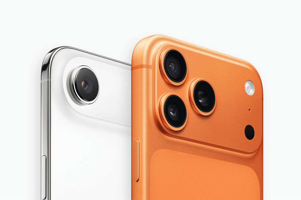 Close-up of the rear cameras on two smartphones—one white with a single lens, the other orange with three lenses and a flash—highlighting Apple moving luxury away from the Pro line in this Air vs Pro comparison.