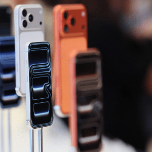 Several new smartphones in various colors are displayed upright on stands, with their screens facing forward. The background is blurred, drawing focus to the phones amid discussions around Apple EU antitrust regulations.