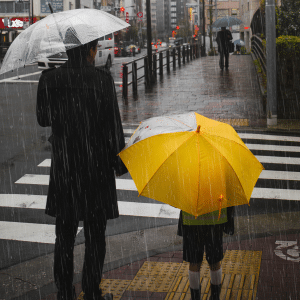An adult and a child holding umbrellas, one clear and one bright yellow, cross a city street in the rain. Rain streaks are visible as iOS 26 weather route alerts guide their way, with the crosswalk and wet pavement reflecting the urban surroundings.