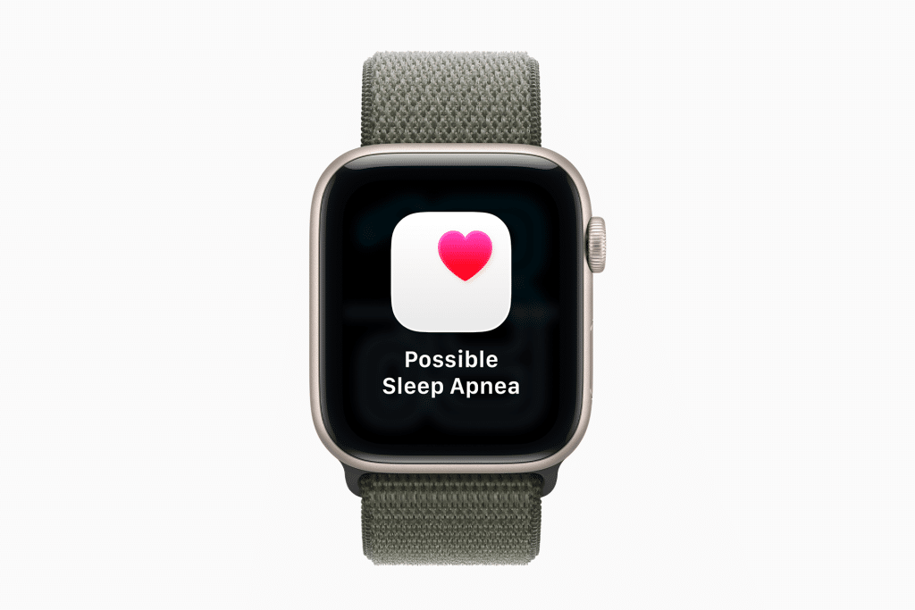 A smartwatch with a green fabric band displays a screen showing a heart icon and the text "Possible Sleep Apnea" on a black background, highlighting advanced features like hypertension alerts.