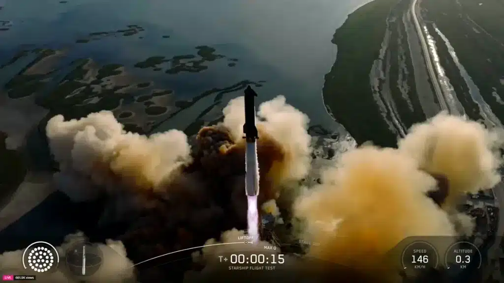 A rocket launches, surrounded by clouds of smoke, over a coastal area with water and greenery visible during the SpaceX 11th Starship test flight. On-screen data shows a speed of 146 and altitude of 0.3, with a timer at T+00:00:15.