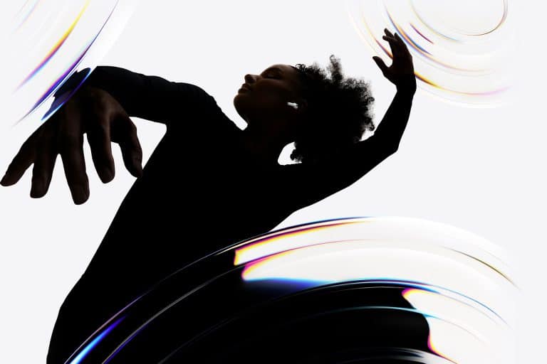 A person in a black outfit dances gracefully with arms raised, surrounded by swirling, translucent, rainbow-tinted shapes on a white background.