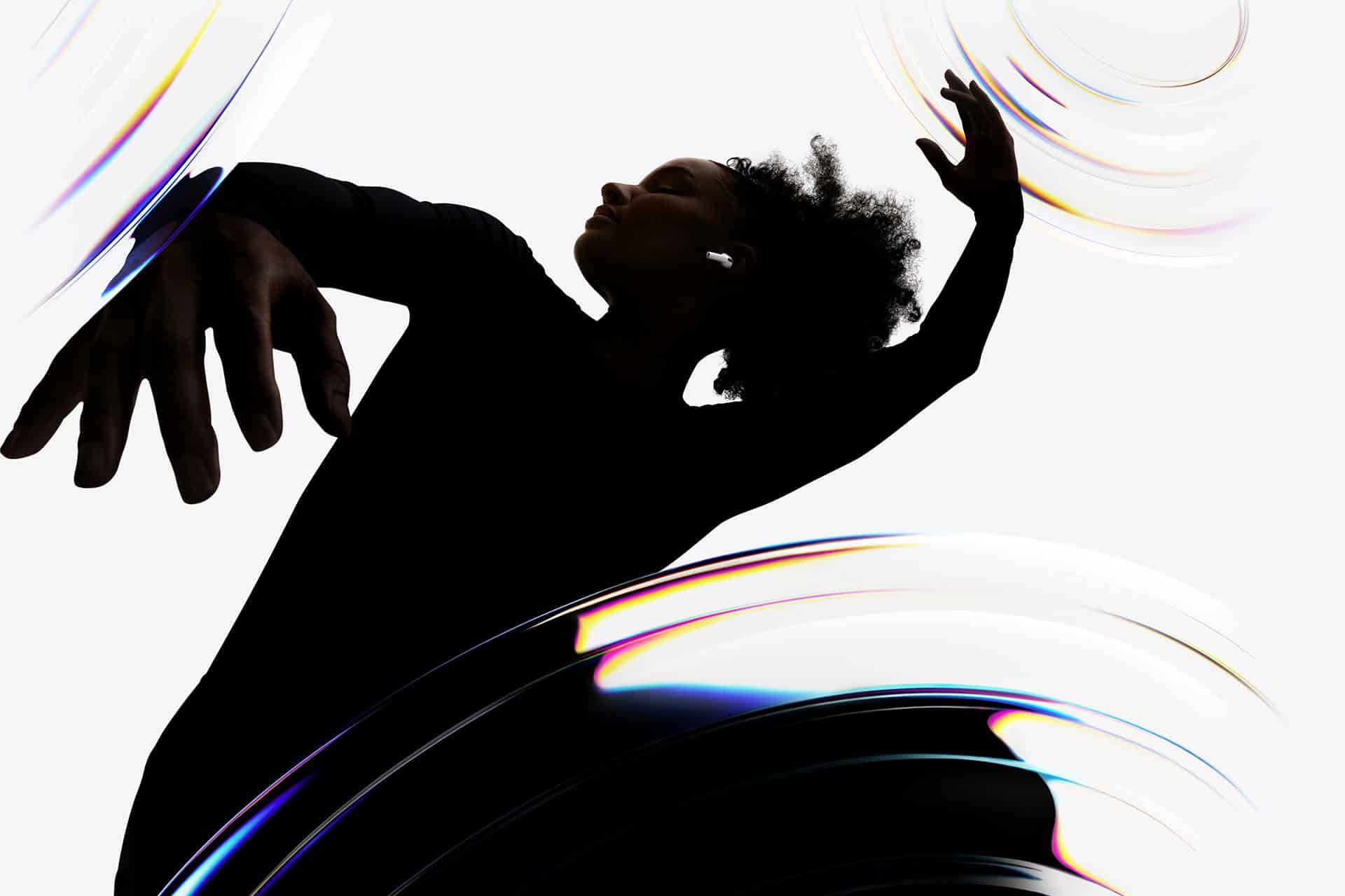 A person in a black outfit dances gracefully with arms raised, surrounded by swirling, translucent, rainbow-tinted shapes on a white background.